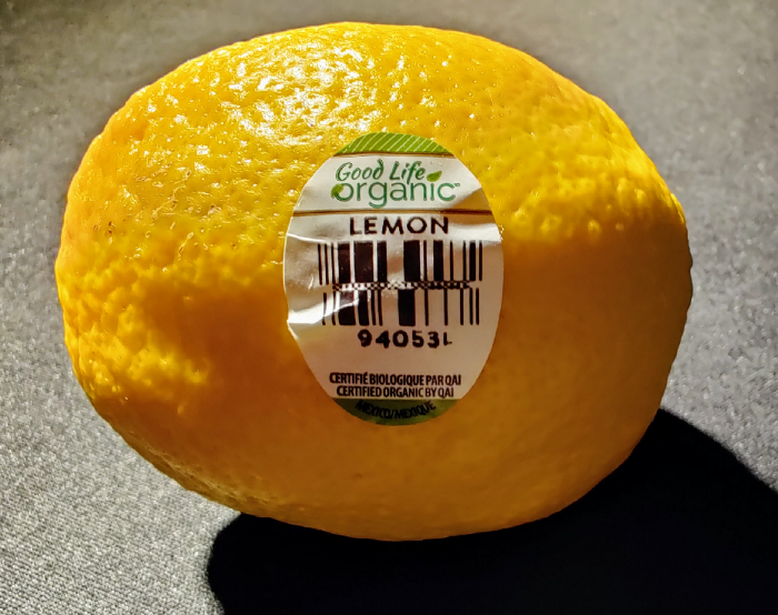 A lemon carrying an organic certification sticker, printed with a barcode and a product number